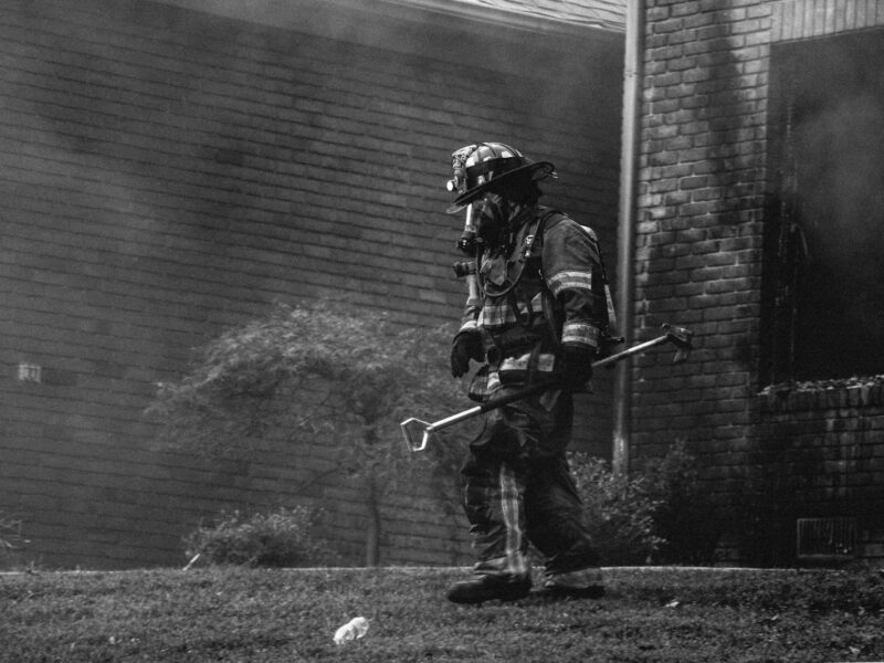 grayscale photography of firefighter holding equipment near houses